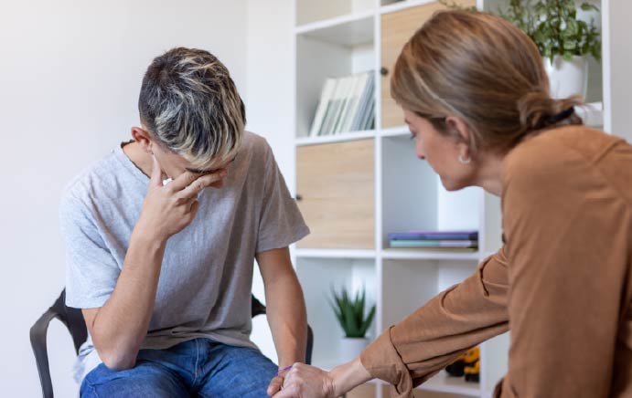 A young person holding their head while a psychiatrist holds their hand